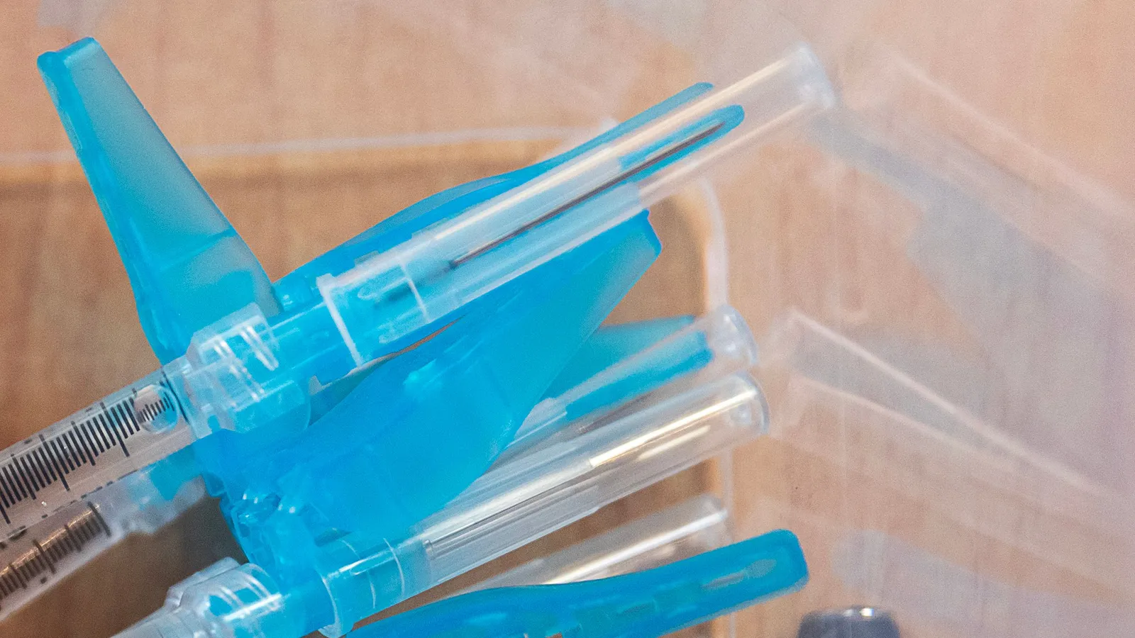 Zużyte strzykawki z niebieskimi osłonkami igieł w plastikowym pojemniku